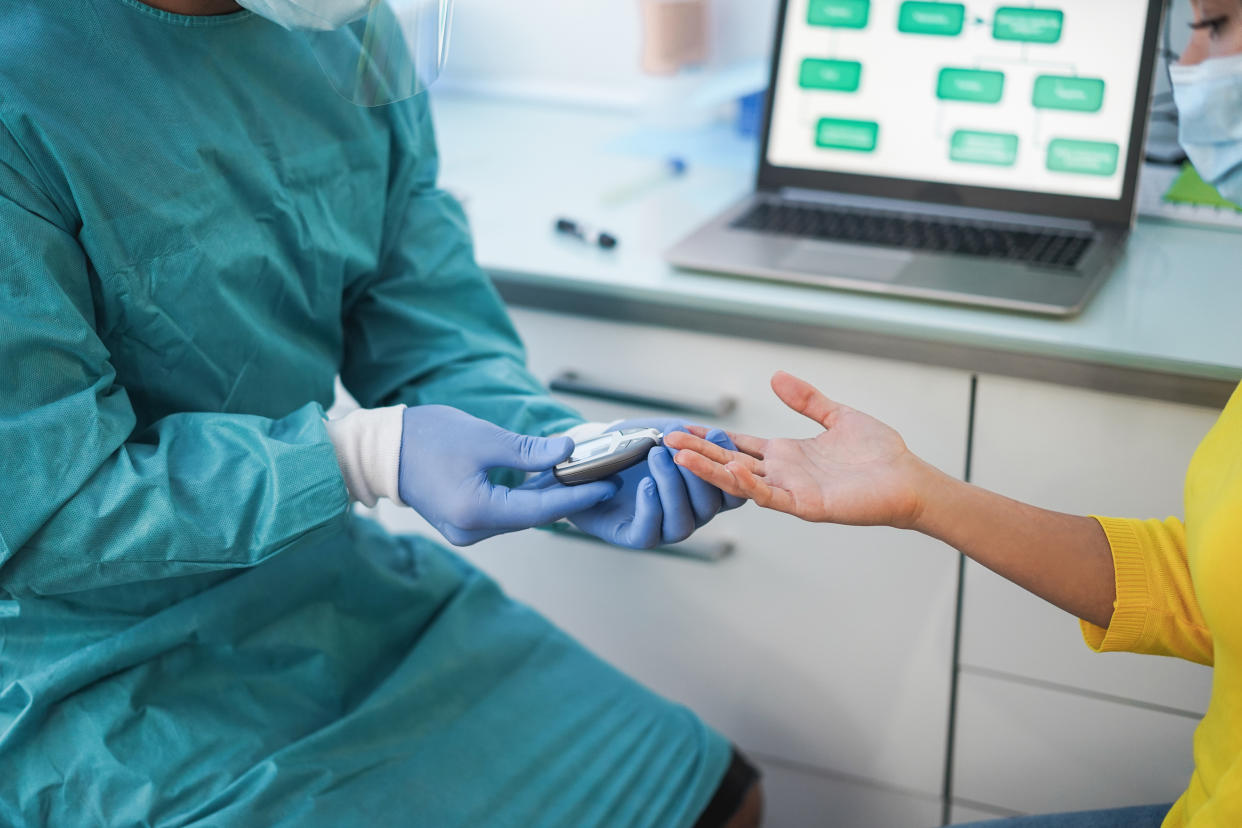 Doctor making blood glycemia test to young woman in medical clinic for diabetes - Medical worker and patient wearing surgical face masks for coronavirus prevention