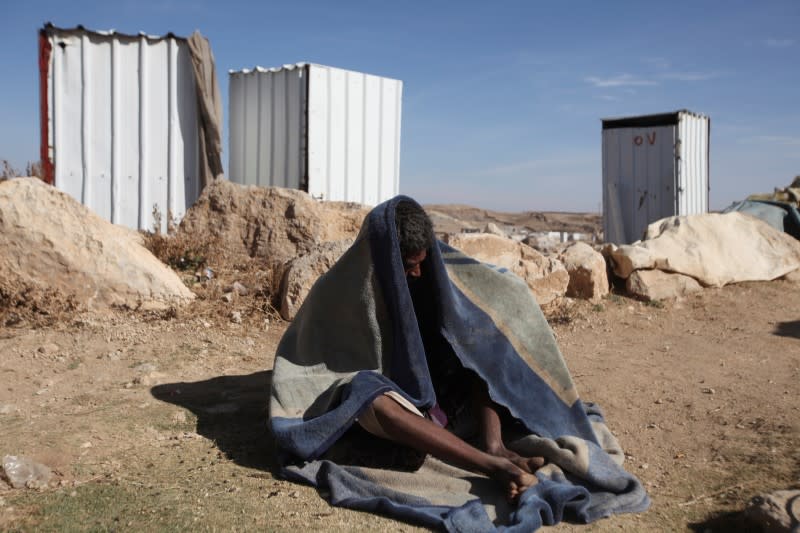 Man covers himself with a blanket as he sits in the sun at a camp for internally displaced people in Khamir of the northwestern province of Amran