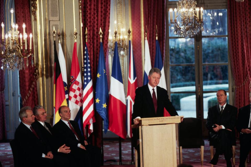 Former President Bill Clinton stands behind a lectern surrounded by leaders of several countries.