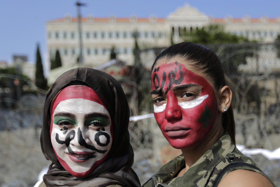 Anti-government protesters with the colors of the Lebanese national flag painted on their faces and with Arabic that reads "Revolution," pose for a photograph in front of the government palace in Beirut, Lebanon, Monday, Oct. 21, 2019. Protesters have closed major roads around Lebanon ahead of an emergency Cabinet meeting to discuss a rescue plan for the country's crumbling economy. AP Photo/Hassan Ammar)