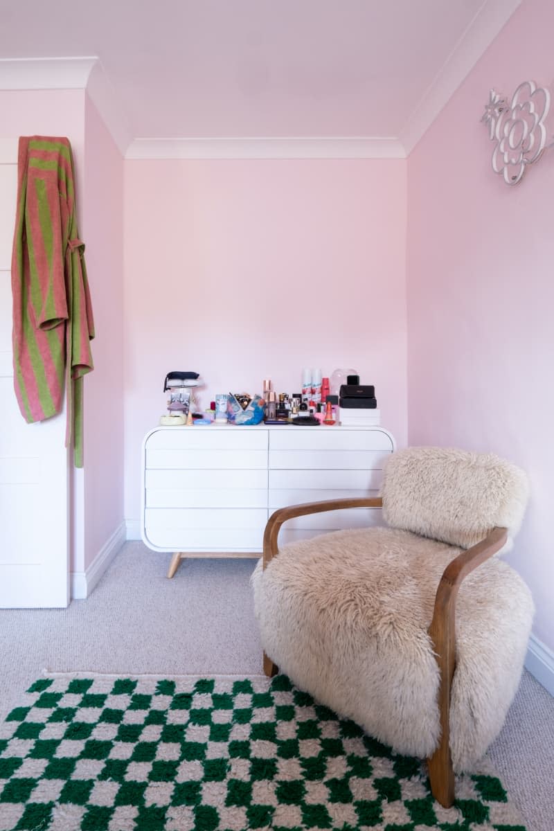 Furry chair and white dresser are seen in nook of pink bedroom.