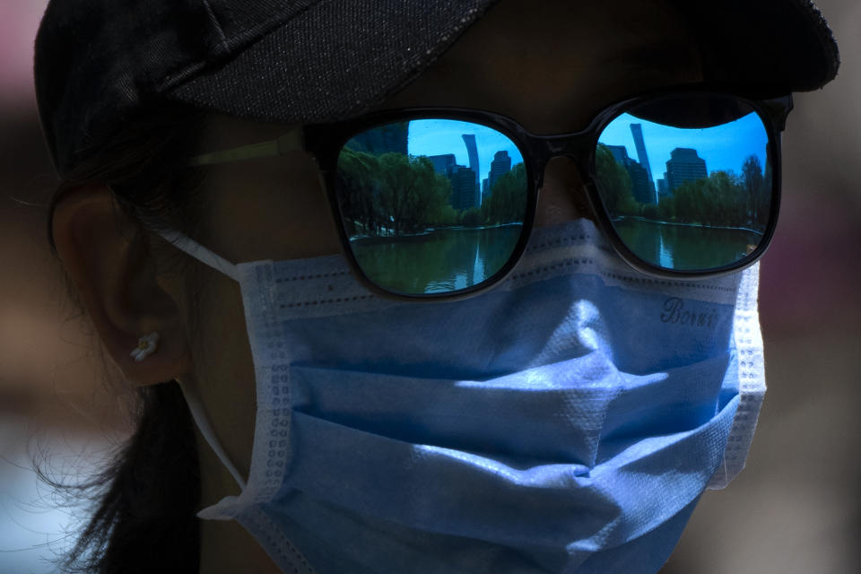 The skyline of Beijing is reflecting in the sunglasses of a woman wearing a face mask as she walks at a public park in Beijing, Thursday, April 14, 2022. (AP Photo/Mark Schiefelbein)