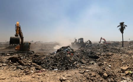 Municipal workers drive shovel machines to extinguish fires inside the garbage at a rubbish dump in Baghdad