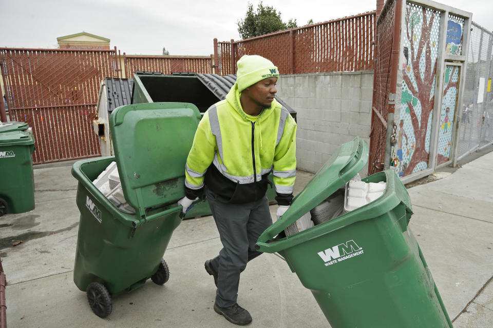 In this photo taken Thursday, Oct. 27, 2016, apprentice garbage man Corey Lever collects trash outside a school in Oakland, Calif. A new partnership between Waste Management of Alameda County Inc., the nonprofit Oakland Civicorps and unions gives young adults, often high school dropouts from low-income communities, a chance to become teamster drivers after two years of training. Like most little boys, Lever liked trucks, but his favorite was always the garbage truck. (AP Photo/Eric Risberg)