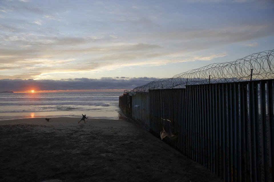 ARCHIVO - En esta fotografía del 9 de enero de 2019 un hombre le lanza una pelota a su perro junto a un muro fronterizo en Tijuana, México. (AP Foto/Gregory Bull, Archivo)