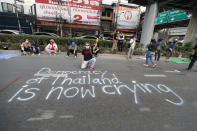 An anti-government protester flashes the three finger protest gesture while kneeling behind a slogan written on the road during a rally Wednesday, Dec. 2, 2020, in Bangkok, Thailand. Thailand's highest court Wednesday acquitted Prime Minister Prayuth Chan-ocha of breaching ethics clauses in the country's constitution, allowing him to stay in his job. (AP Photo/Sakchai Lalit)