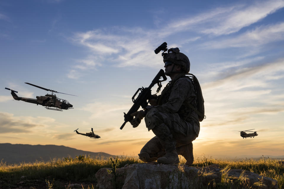 Military Helicopters flying behind kneeling soldier at sunset