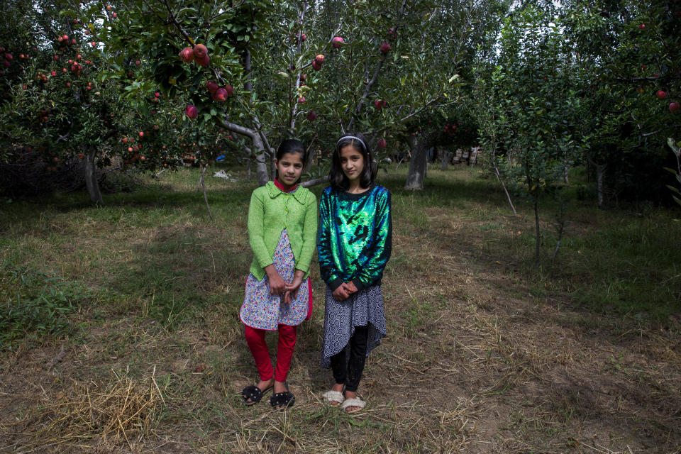 In this Oct. 6, 2019, photo, twin sisters Tabeer Shafi Bhat, right, and Taseer Shafi Bhat stand for photographs inside an apple orchard in Wuyan, south of Srinagar, Indian controlled Kashmir. The girls said that they've had nothing to do since the lockdown started on Aug. 5 and that they miss going to school. Authorities encouraged students to return to school but parents have largely remained unwilling to send their kids to educational institutes due to the restrictions in place. (AP Photo/ Dar Yasin)