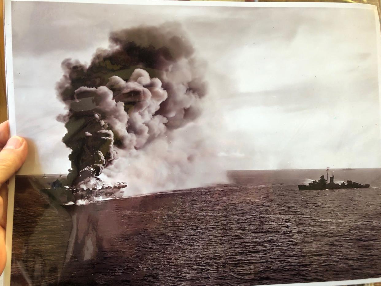 Joe Cooper holds up a photo of the USS Ommaney Bay blowing up after being attacked by a kamikaze.