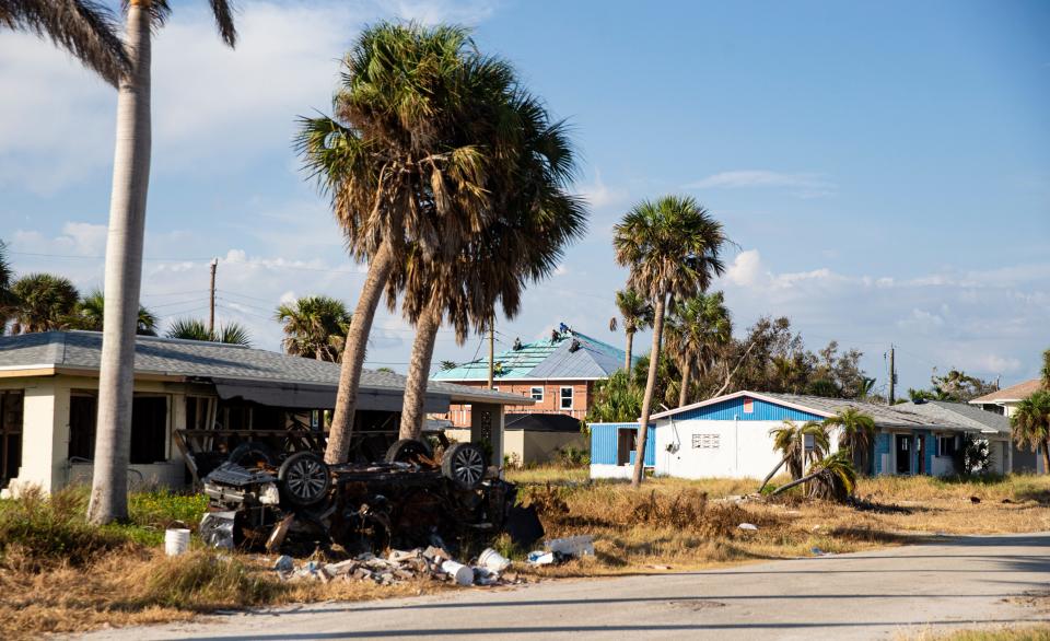 Roofers work on a home on Fort Myers Beach while a destroyed vehicle left from Hurricane Ian sits in a neighborhood on Fort Myers Beach on Thursday, Sept. 7, 2023. The town was decimated in the Hurricane that hit Sept. 28 of last year.