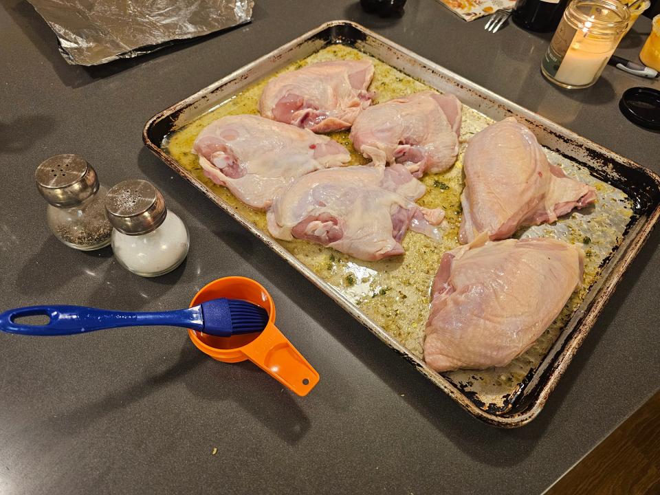 Raw chicken on cooking sheet next to pastry brush in container and salt and pepper shakers