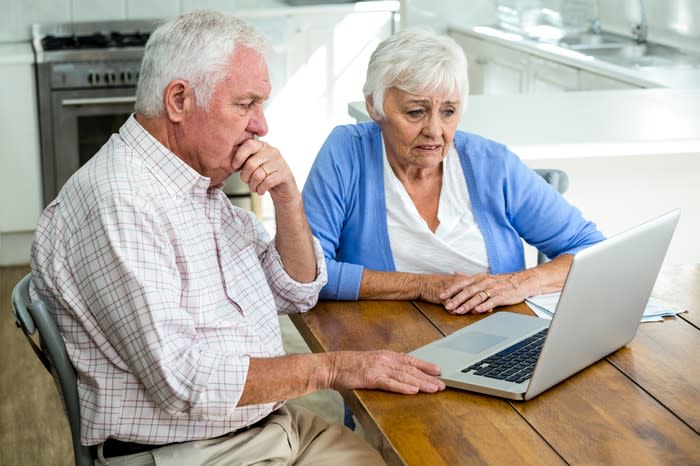 Senior couple seated at a table, staring at a laptop with worried expressions