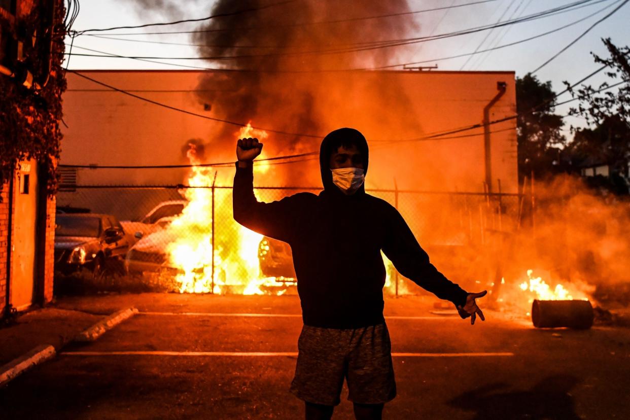 A protestor gestures as cars burn behind him during a demonstration in Minneapolis: AFP via Getty Images