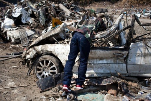 A tsunami survivor finds his car amongst the debris in the town of Minamisanriku in Miyagi prefecture. The impact of Japan's earthquake and nuclear crisis rippled through the economy as the government downgraded its outlook and Toyota announced more temporary plant shutdowns overseas