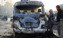 In this photo released by the Syrian official news agency SANA, Syrian security officers gather around a burned bus at the site of a deadly explosion, in Damascus, Syria, Wednesday, Oct. 20, 2021. Two roadside bombs exploded near a bus carrying troops during the morning rush hour in the Syrian capital early Wednesday, killing and wounding several people, state TV reported. (SANA via AP)