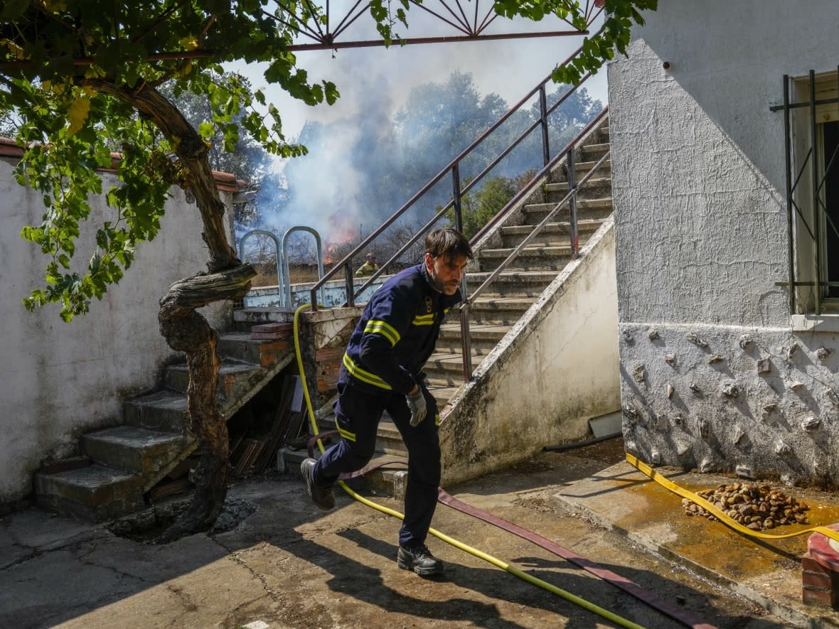 A firefighter works to extinguish a wildfire getting close to a house in Tabara, northwest Spain, in July. (Bernat Armangue/AP - image credit)