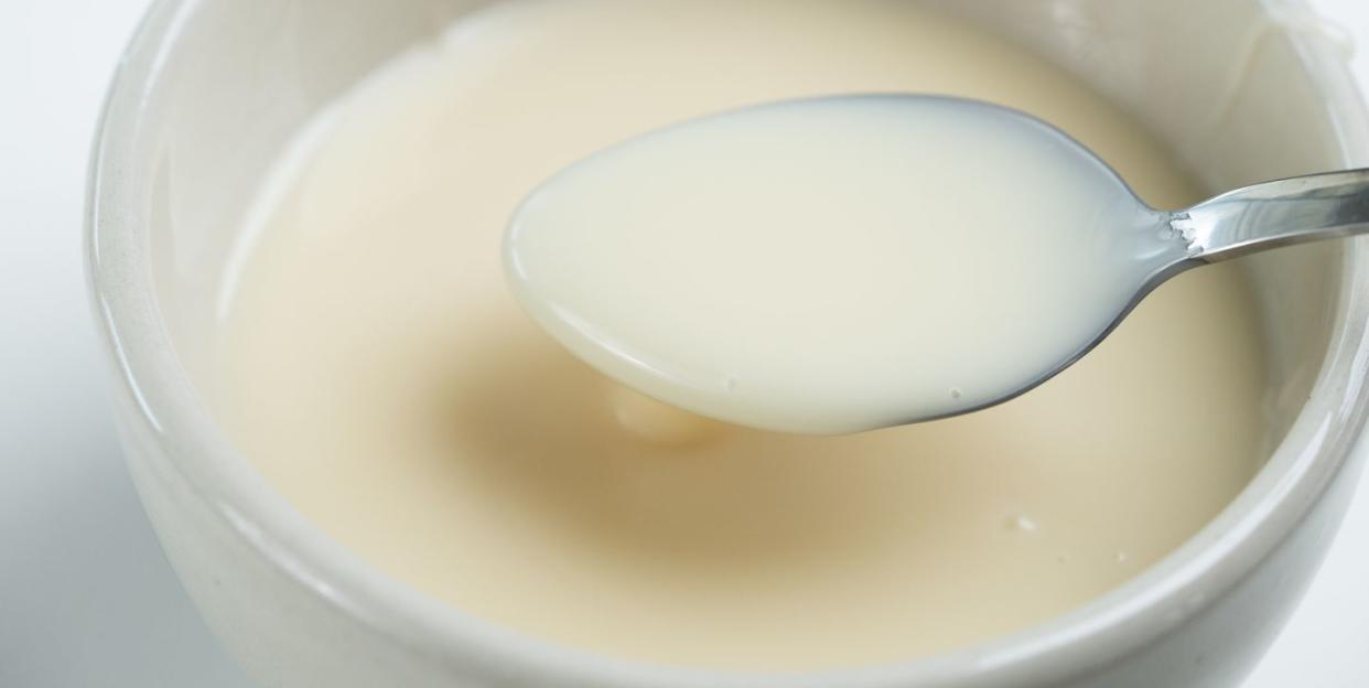 close up of condensed milk with spoon isolated on white background, food ingredients concept