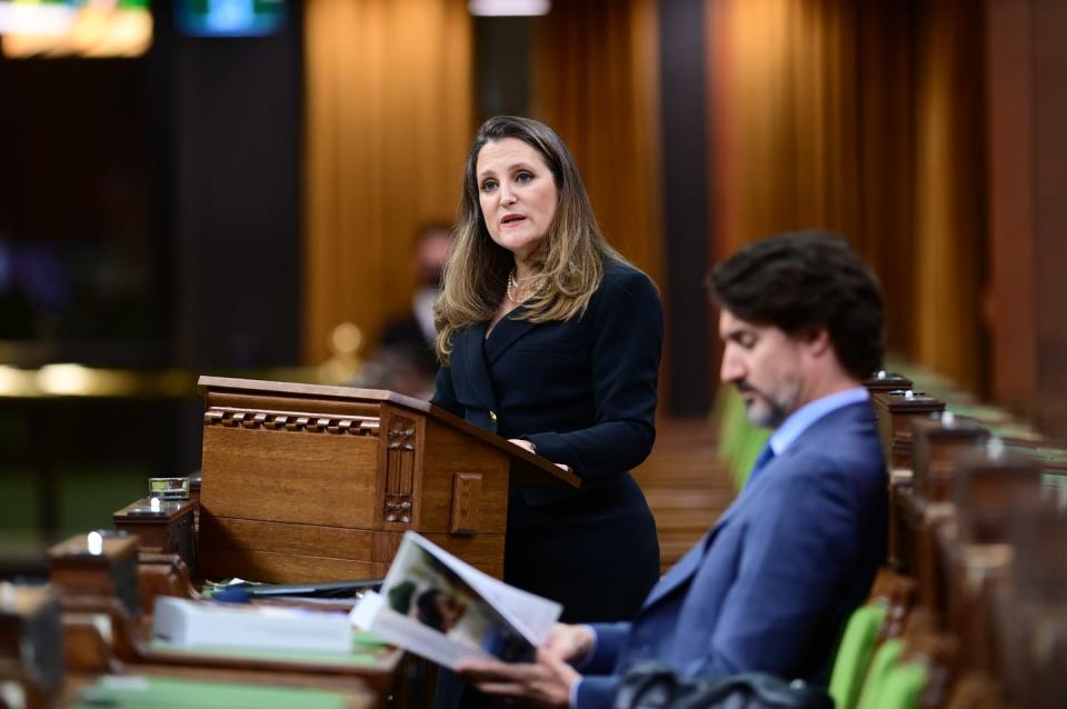 Freeland delivers the budget as Trudeau sits beside her reading the document.