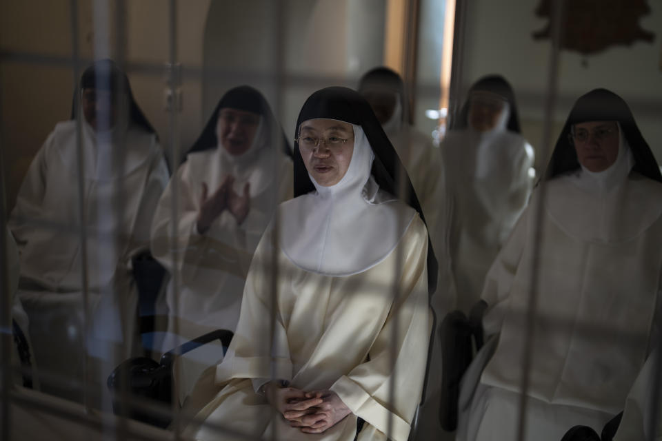 Sister María de la Trinidad, center, and other cloistered nuns speak to journalists from behind a white iron grille in the parlor of the Monastery of St. Catherine on the Greek island of Santorini on Tuesday, June 14, 2022. The convent is home to more than a dozen nuns who devote themselves to prayer and leave only for medical or government necessities. (AP Photo/Petros Giannakouris)