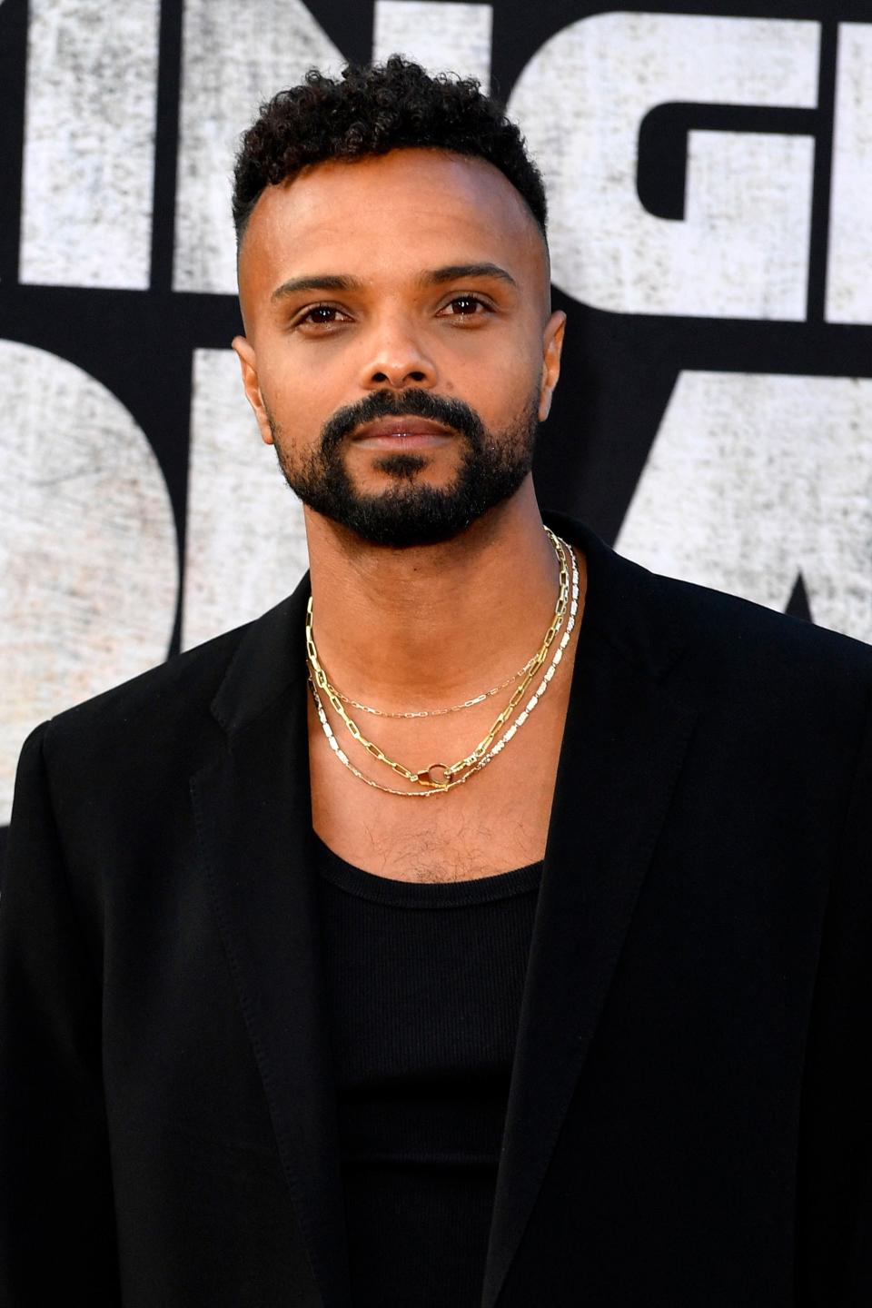 Eka Darville in a black outfit with gold necklaces at the premiere for Kingdom of the Planet of the Apes