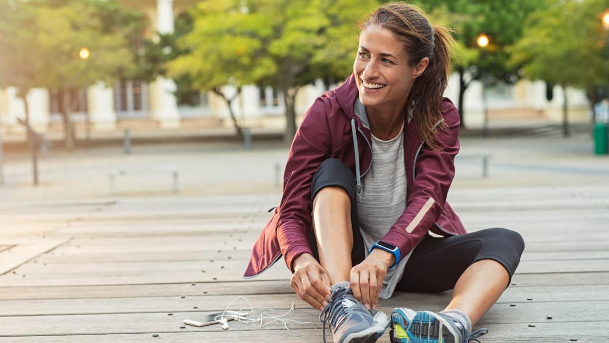 Mature fitness woman tie shoelaces on road.