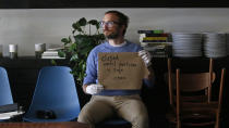 File = This May 7, 2020 file photo, Josh Rosenthal holds a " closed until everyone is safe" sign as he sits in Creek Tea in Salt Lake City. Rosenthal, said the disruption caused by COVID-19 proved to be too much. He's closing his store. Many businesses have been given the green light to reopen, but owners are finding it's not that simple and many may not be able to weather the storm brewed up by COVID-19. (AP Photo/Rick Bowmer)