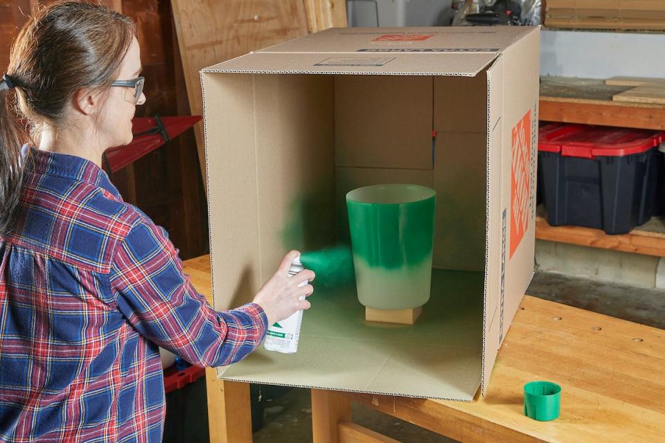 Woman using spray paint to paint a plastic bin green.