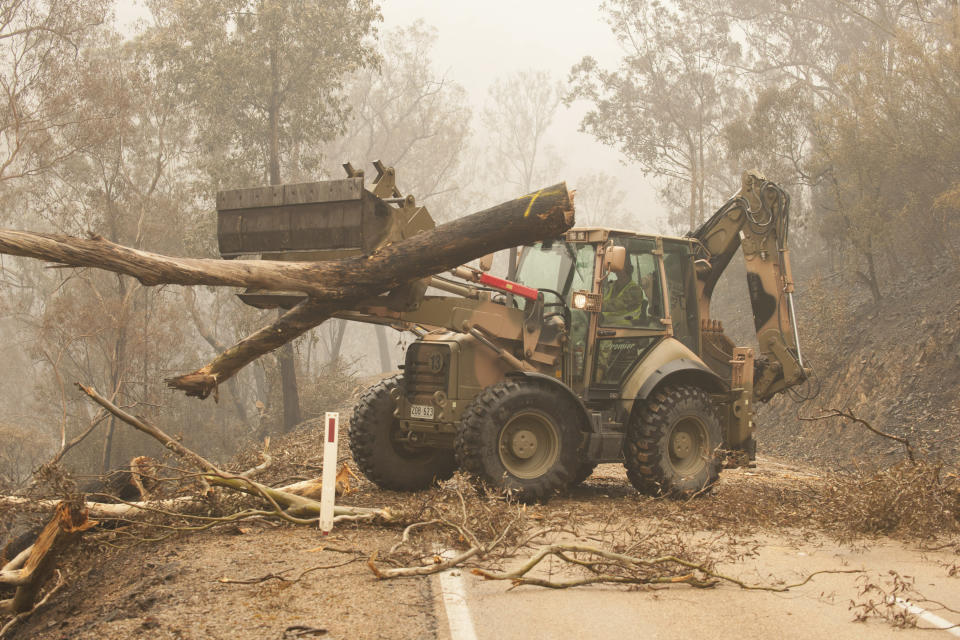 In this image released and dated on Jan. 6, 2020, from Australian Department of Defence, plant operators Cpl. Duncan Keith and Sapper Ian Larner of the 22nd Engineer Regiment use a 434 backhoe to assist staff from Forestry Management Victoria to clear fire damaged trees from the great Alpine road between Bairnsdale and Omeo during Operation Bushfire Assist 19-20 in Bairnsdale, Victoria, Australia. Australia's government on Monday said it was willing to pay “whatever it takes” to help communities recover from deadly wildfires that have ravaged the country. (Department of Defence via AP)