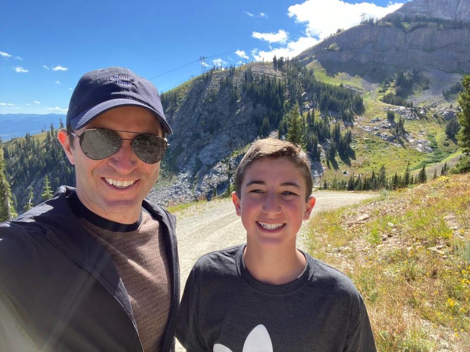 Robert Bronstein with his teenage son, Nate, pose in front of wooded mountains.