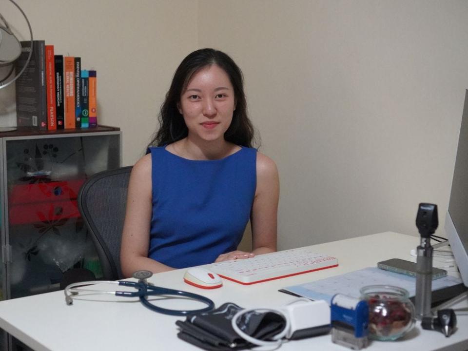 Faith Choo sitting at her desk with her stethoscope and medical devices sprawled across the table.