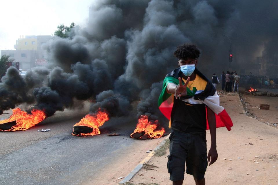 A Sudanese protester draped with the national flag flashes the victory sign next to burning tyres during a demonstration in the capital Khartoum, on October 25, 2021.