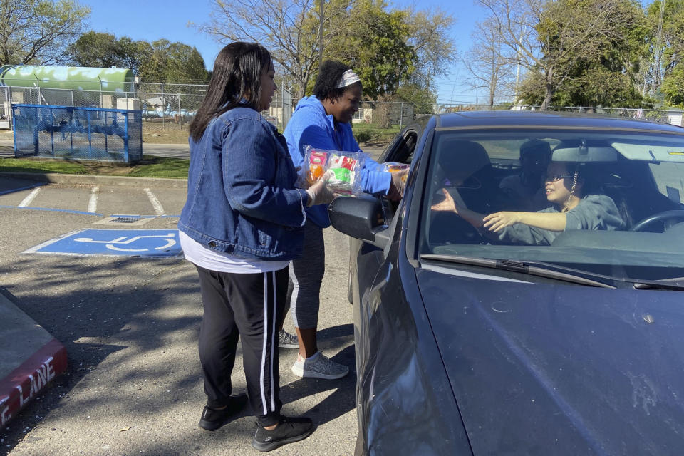 In this Tuesday, March 10, 2020, photo, Florin Elementary School staff hand out food to students and parents driving in, after their facility closed in response to the coronavirus Sacramento, Calif. (AP Photo/Cuneyt Dil)