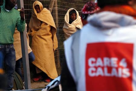 An aid worker provides assistance near a group of migrants claiming to be minors who use blankets to protect themselves from the cold as they prepare to spend the night after the dismantlement of the "Jungle" camp in Calais, France, October 27, 2016. REUTERS/Pascal Rossignol