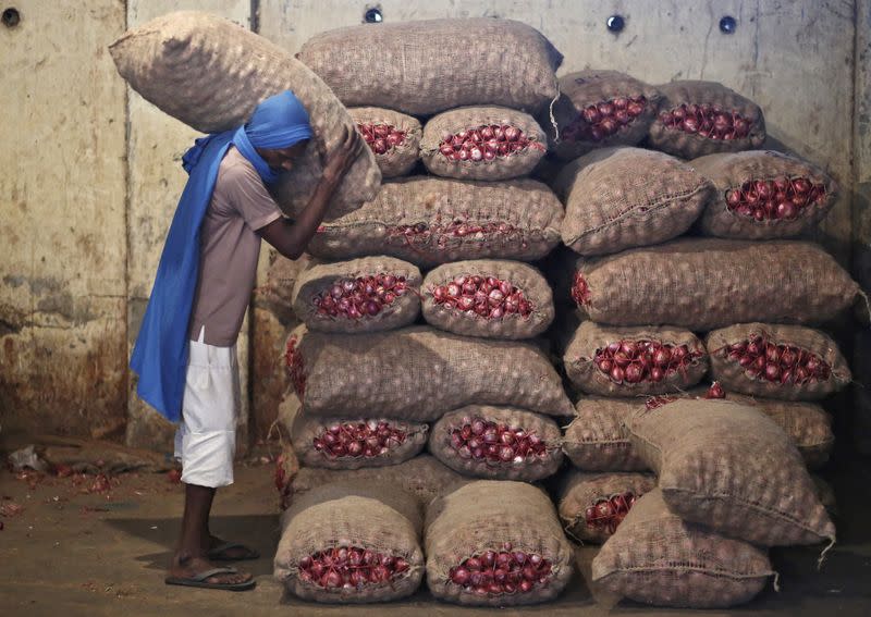 A labourer stacks a sack of onions in a storage room at a wholesale vegetable and fruit market in New Delhi