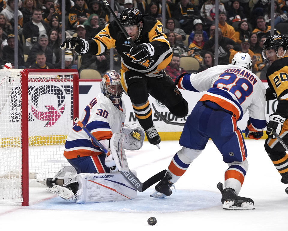 Pittsburgh Penguins' Bryan Rust (17) leaps across the goal crease between New York Islanders goaltender Ilya Sorokin (30) and Islanders' Alexander Romanov (28) during the second period of an NHL hockey game in Pittsburgh, Tuesday, Feb. 20, 2024. (AP Photo/Gene Puskar)