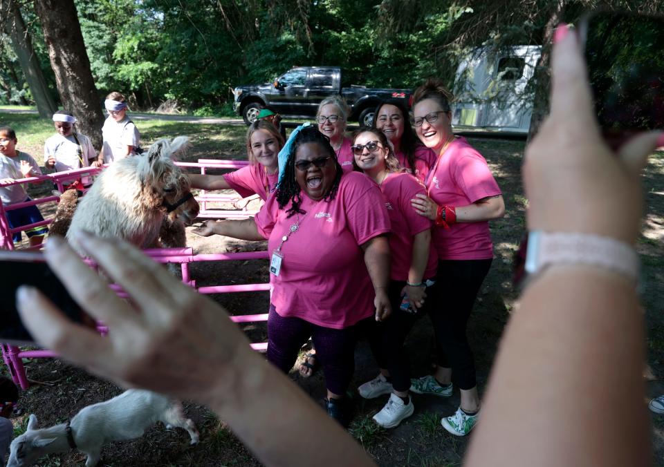 Members from Angela Hospice Center in Livonia laugh when having pictures taken with Tony the Llama during the second annual Camp Monarch run by the center at the Madonna University Welcome Center in Livonia on August 4, 2023. 
The two-day camp is for children ages 5 to 17 who have experienced the loss of a loved one to allow them to bond with other kids their age, talk about grief and get consoling from adults.