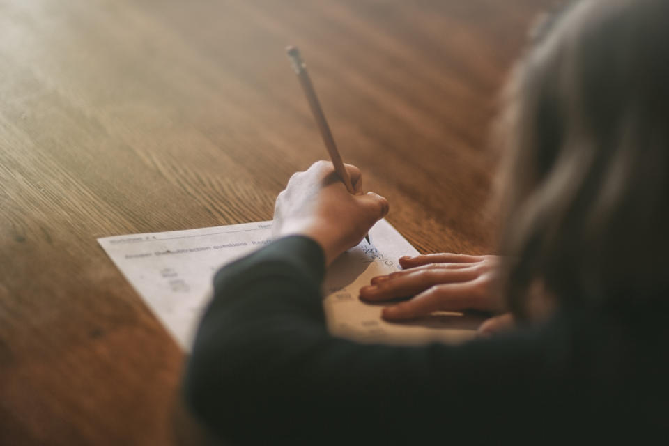 Person writing on paper, possibly budgeting or planning, with focus on their hand and pen