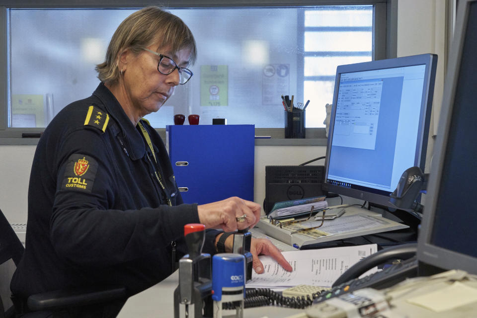 Chief Customs officer Nina Bullock was handling traditional paper clearance forms on Friday, Feb. 8 2019 as her computer informed her of an incoming truck using a new digital customs clearance system that allows transporters to drive through customs without stopping. Norway's hard border with the European Union is equipped with cameras, license-plate recognition systems and barriers directing traffic to Customs officers. (AP Photo/David Keyton)