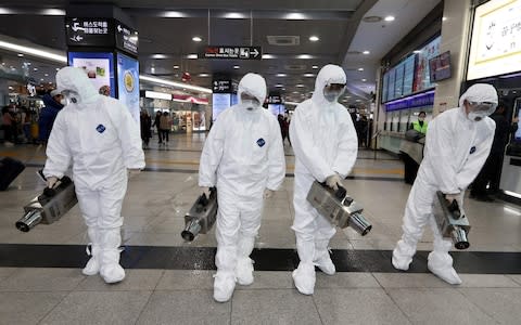 Health workers wearing protective gears spray disinfectant as part of efforts to prevent the spread of a new virus which originated in the Chinese city of Wuhan, at a bus terminal in Gwangju  - Credit: AFP