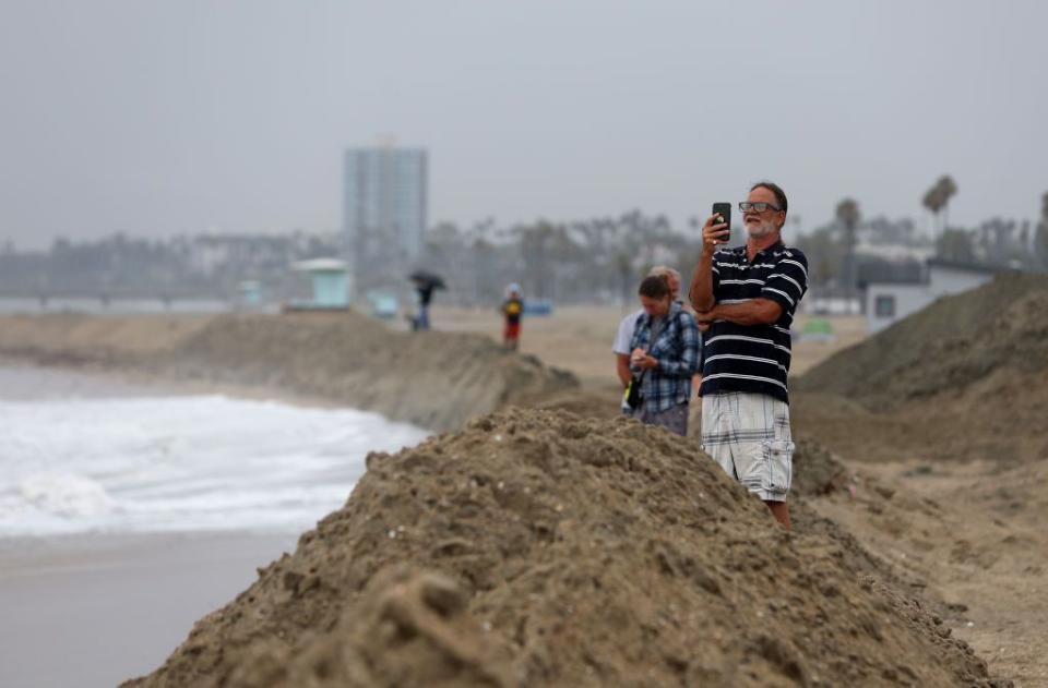 People stand on a sand berm at Belmont Shore Beach as tropical storm Hilary approaches Southern California.