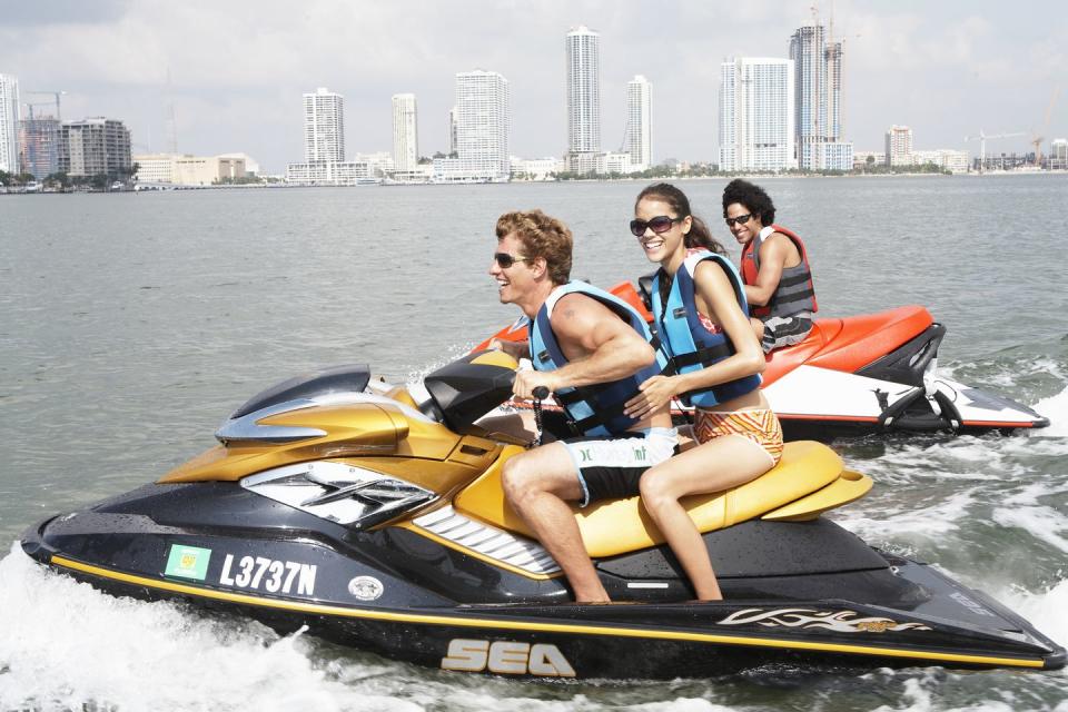 three people on jet boats, city skyline in background, side view