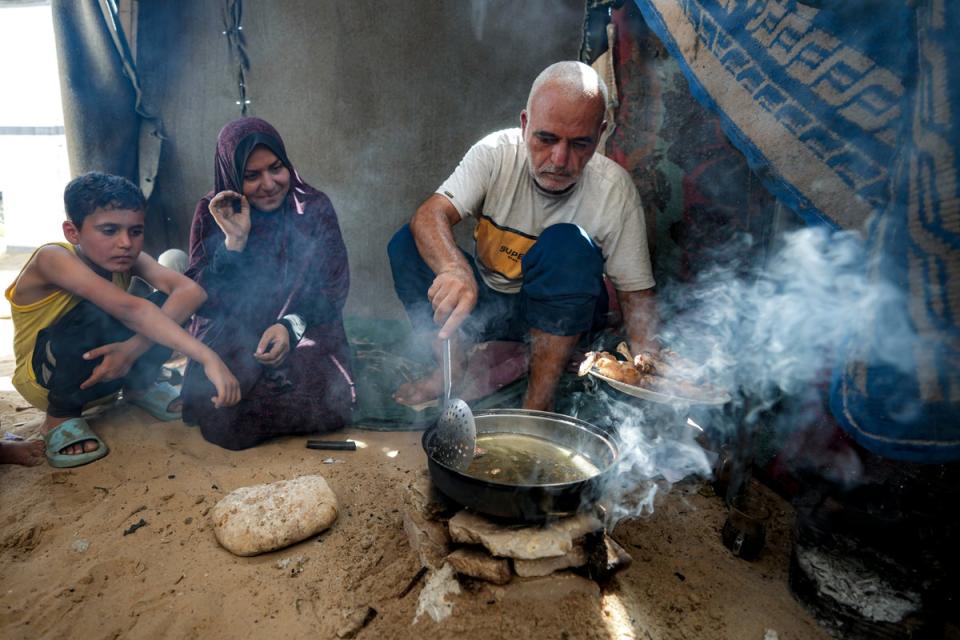 Hassan Nofal, right, who was displaced by the Israeli bombardment of the Gaza Strip, prepares lunch with his family at a makeshift tent camp in Khan Younis (AP)