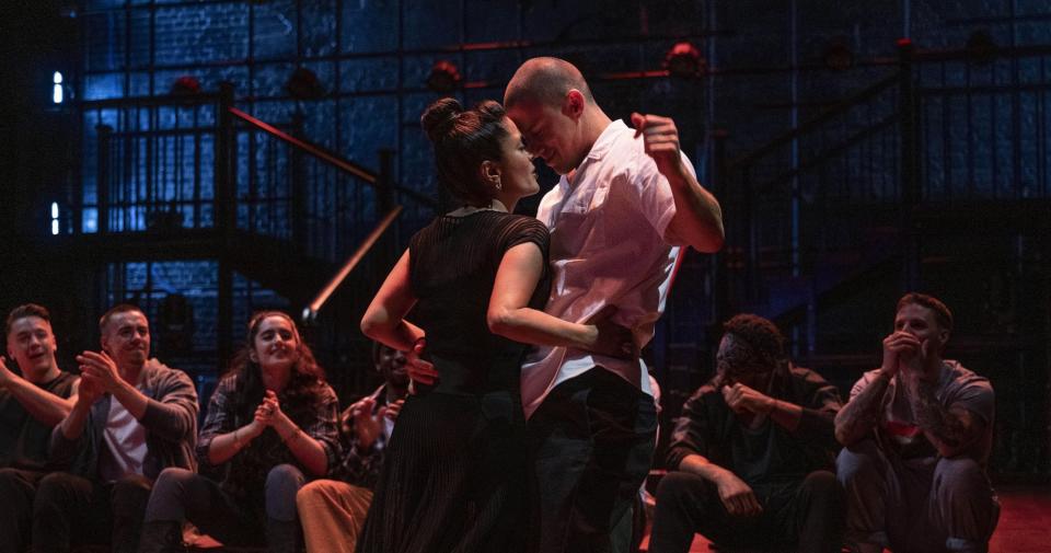 A man dances intimately with a woman near a group of observant dance students