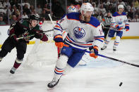 Edmonton Oilers defenseman Mattias Ekholm (14) skates with the puck in front of Arizona Coyotes center Logan Cooley, left, during the first period of an NHL hockey game Wednesday, April 17, 2024, in Tempe, Ariz. (AP Photo/Ross D. Franklin)