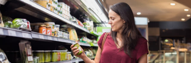 woman shopping at the grocery store and holding up a jar of something to read