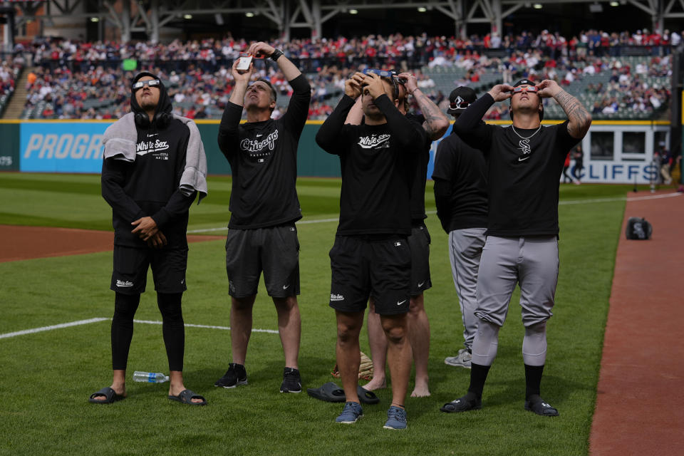 Members of the Chicago White Sox look up from the grass outside the dugout as the moon partially covers the sun during a total solar eclipse over Progressive Field in Cleveland, Monday, April 8, 2024, before the Cleveland Guardians home opener baseball game. (AP Photo/Carolyn Kaster)
