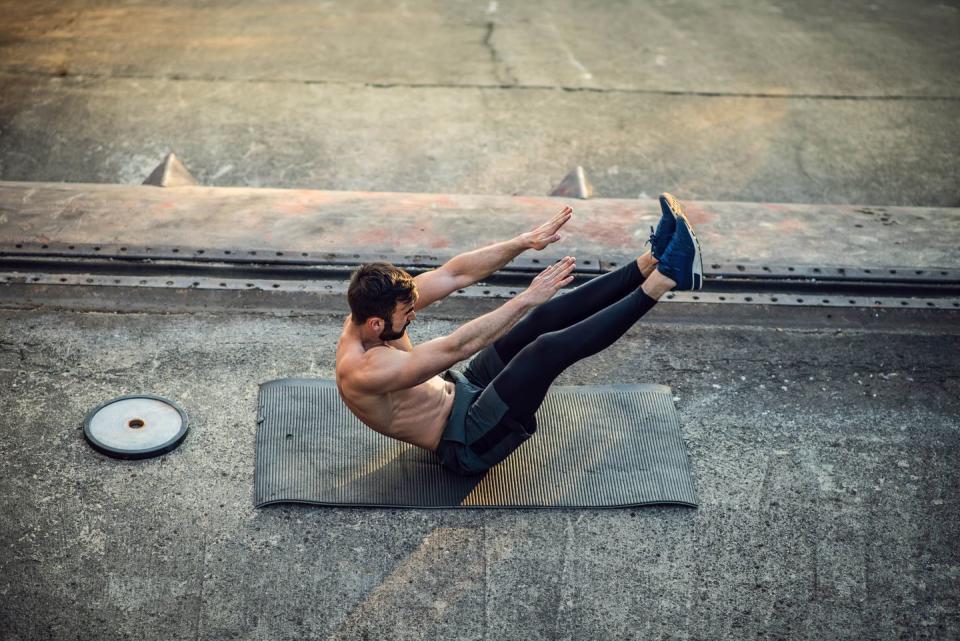 young shirtless muscular man training with weights outdoors at the sunset