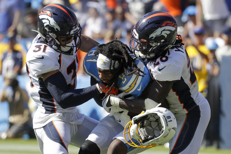 Denver Broncos free safety Justin Simmons, left, and cornerback Isaac Yiadom, right, tackle Los Angeles Chargers wide receiver Mike Williams as he looses his helmet during the first half of an NFL football game Sunday, Oct. 6, 2019, in Carson, Calif. (AP Photo/Alex Gallardo)