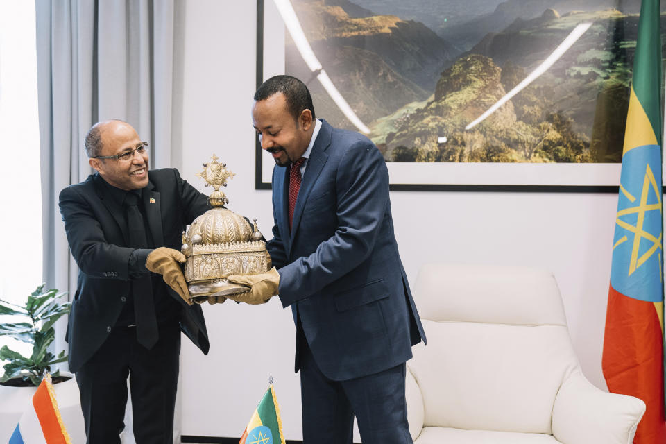 Ethiopia's Prime Minister, Abiy Ahmed, right, with gloved hands as he officially hands over a crown to the country's tourism minister, Hirut Kassaw, Thursday, Feb. 20, 2020. The 18th Century Ethiopian crown has been returned home after being hidden in a Dutch flat for the past 21-years. (The Office of Prime Minister Abiy Ahmed via AP)