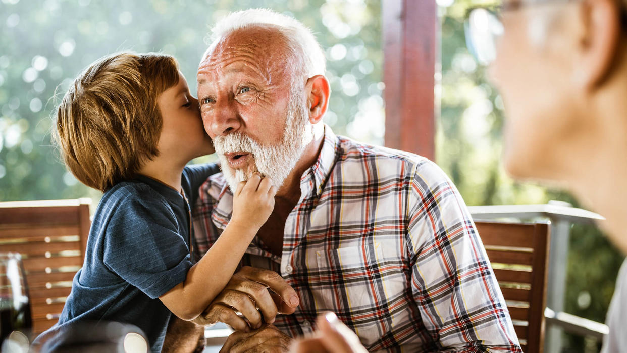 Surprised senior man listening a secret that his grandson is whispering to him during a meal on a terrace.